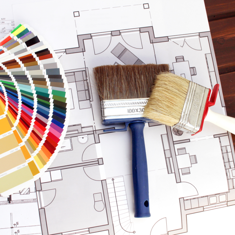 Interior design planning in action â€” architectural blueprints accompanied by paintbrushes and a color swatch palette, symbolizing the creative process of selecting materials, colors, and layout during renovation consultation and design services.