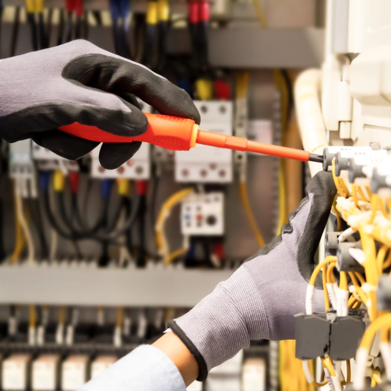 Licensed electrician performing detailed work on an open electrical panel â€” close-up of gloved hands using a screwdriver to adjust colored wiring and components, emphasizing professional electrical installation and safety.