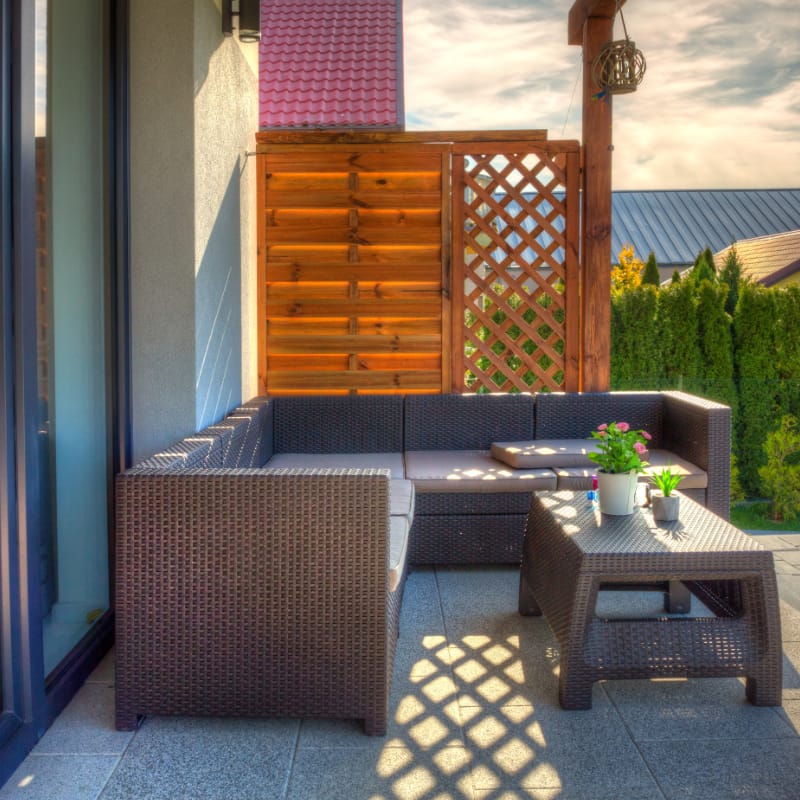 Inviting outdoor terrace with a stylish wicker sectional sofa, beige cushions, and a wooden privacy screen, surrounded by lush greenery â€” showcasing elegant exterior design perfect for relaxation and entertainment.