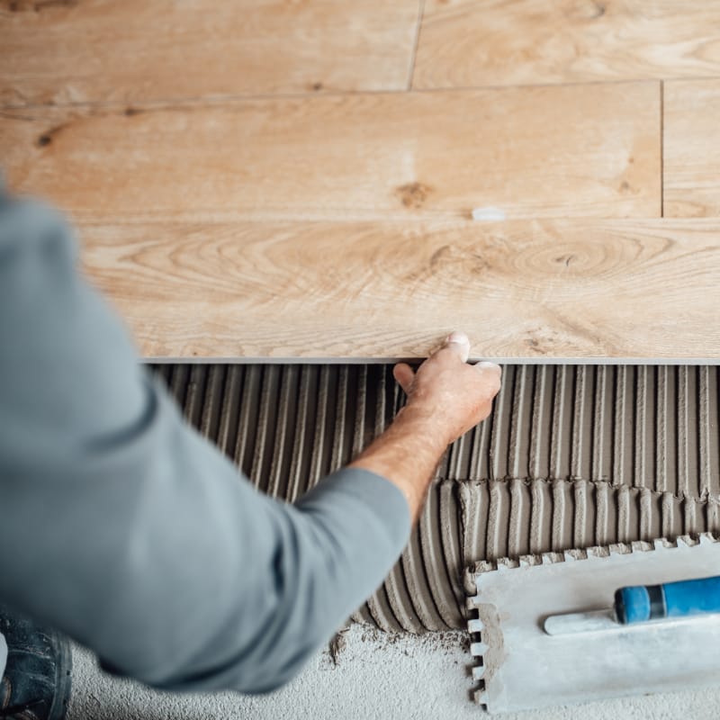 Professional tile and flooring installation in progress â€” close-up of hands placing a wooden plank on adhesive, showcasing expert technique and quality materials.