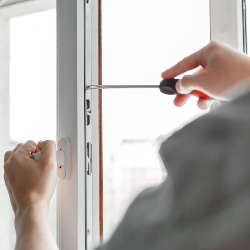 Close-up of a worker using a screwdriver to adjust a modern window frame during installation, highlighting precision craftsmanship and secure fitting as part of professional door and window services.